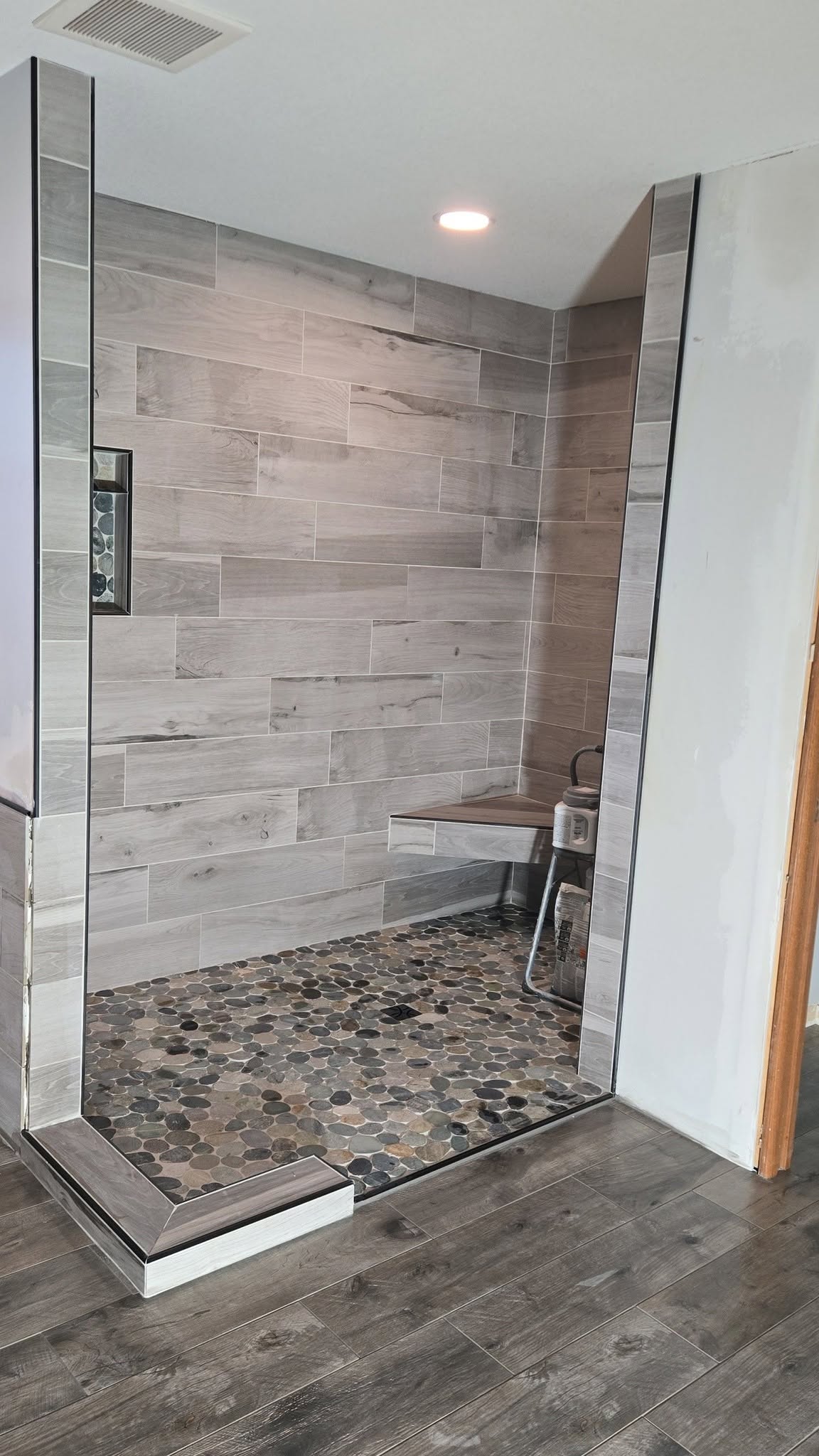Custom tiled walk-in shower with wood-look plank tile and pebble floor